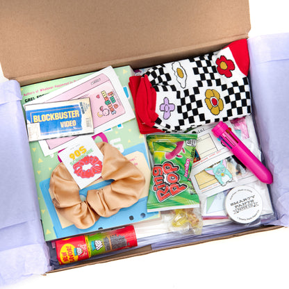 Take a trip down memory lane with our 90s-themed subscription box! This box includes a collection of nostalgia-inducing items like a Furby pin, a stretch yin yang necklace, a Troll ring, a Nightmare on Elm Street pin, ring pop candy, washi tape, fun socks, blockbuster magnnet,and a trendy scrunchie.