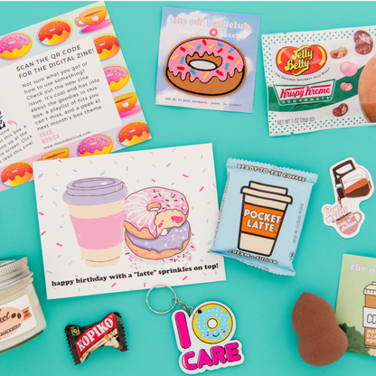 Image of a donut patch and flavored jelly beans, pocket latte chocolate, donut and coffee greeting card, I donut care key chain, Kopiko candy, and a makeup sponge on a blue background. This subscription box is perfect for donut and coffee lovers. Get your sweet fix with our tasty treats and cute accessories. Order now and enjoy your monthly surprise from our team at The Oddball Club.